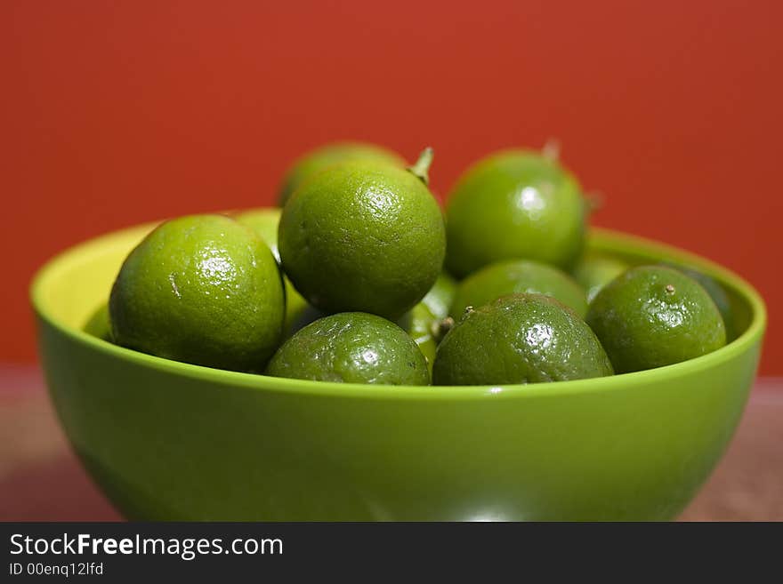 Limes up close in a green bowel against red background.