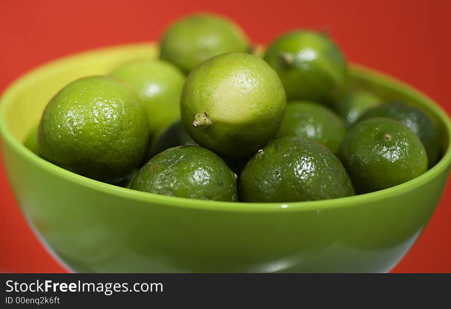 Limes up close in a green bowel against red background.