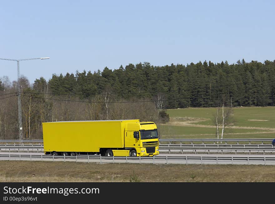 Clean yellow truck driving against spring-green foliage. Clean yellow truck driving against spring-green foliage