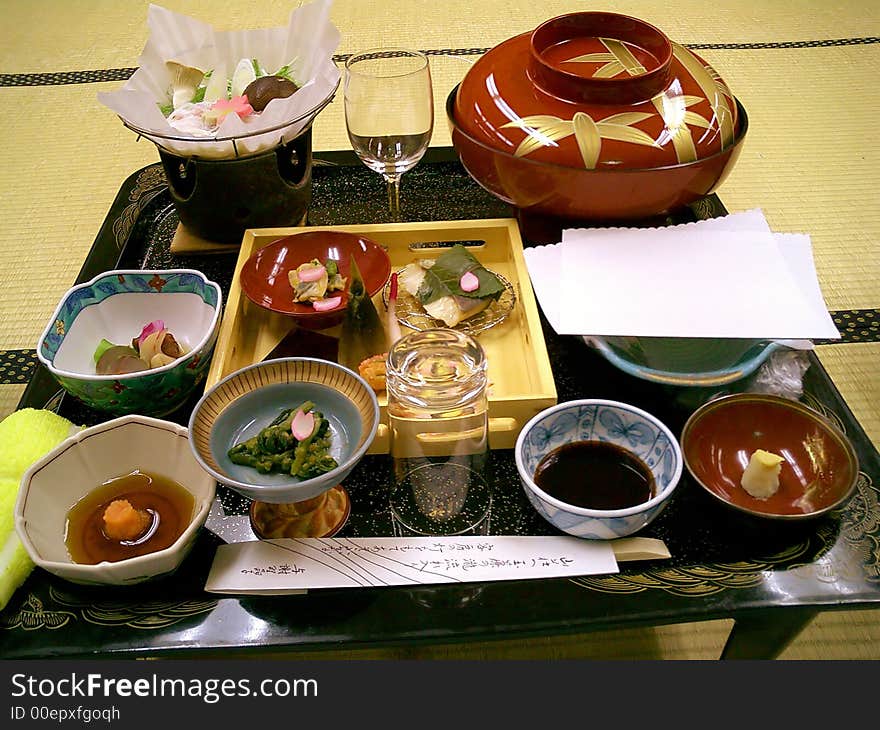 Tray with several different Japanese dishes in bowls, standing on a small low table on bamboo mats