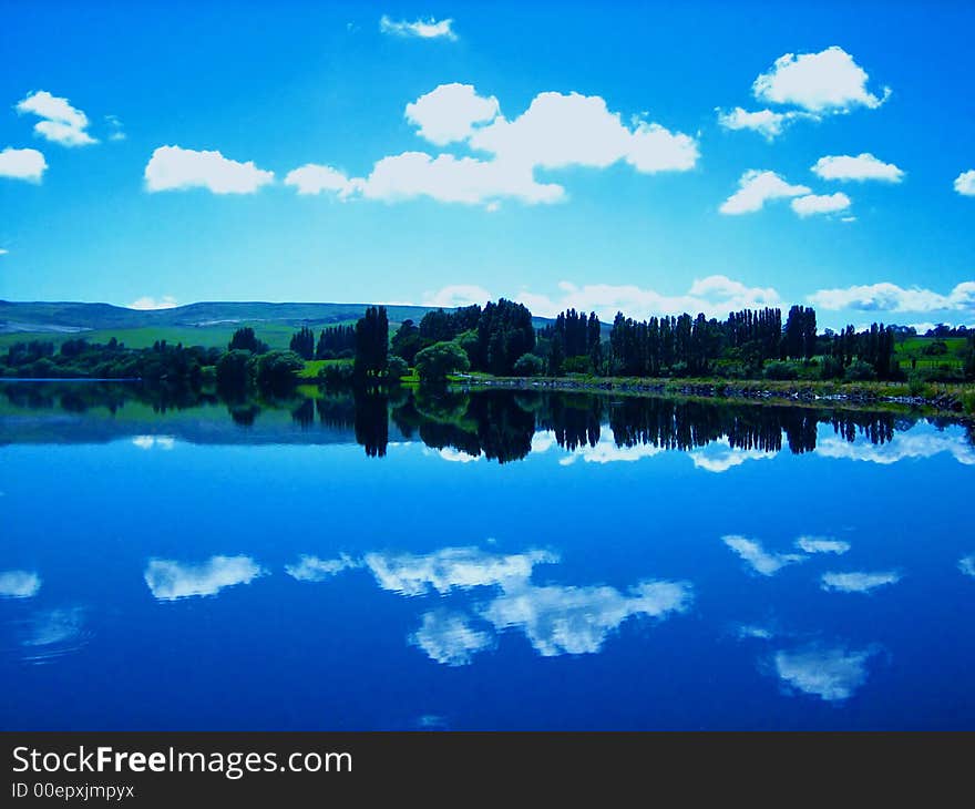 Beautiful blue sky with a few clouds and trees mirrored in calm lake surface. Beautiful blue sky with a few clouds and trees mirrored in calm lake surface