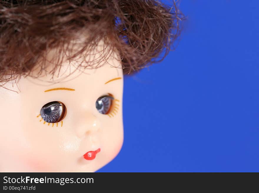 A close up of a doll's face with blue eyes and brown hair. A close up of a doll's face with blue eyes and brown hair