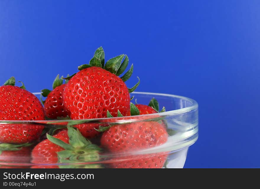 A bowl of organic strawberries with a vibrant blue background