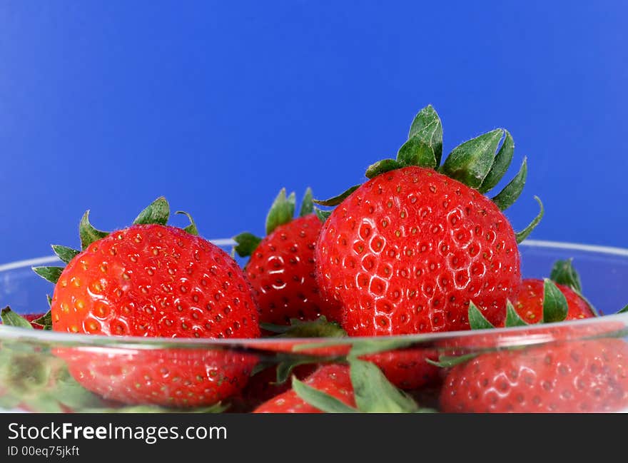 A glass bowl full of organic strawberries with a bright blu background. A glass bowl full of organic strawberries with a bright blu background