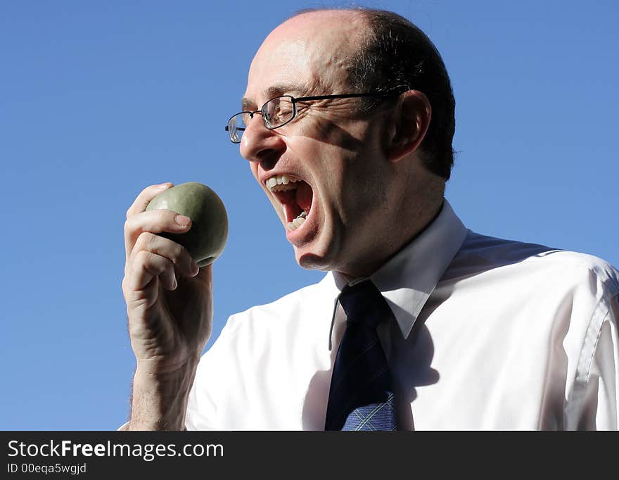 Businessman wearing business clothes about to take a bite into a green apple, showing face, hand, apple and blue sky behind him. Businessman wearing business clothes about to take a bite into a green apple, showing face, hand, apple and blue sky behind him.