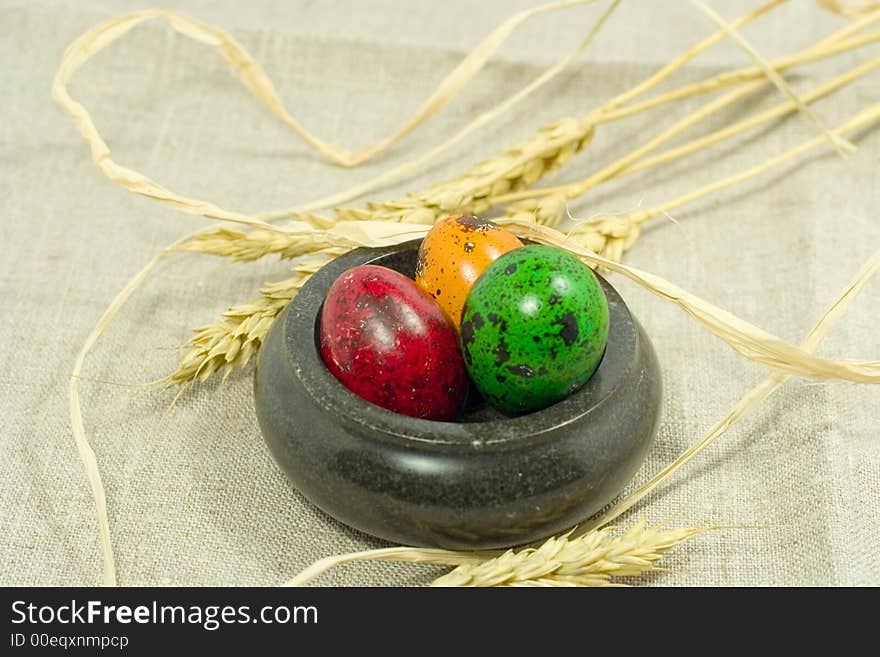 Colorful eggs in bowl and wheat ears