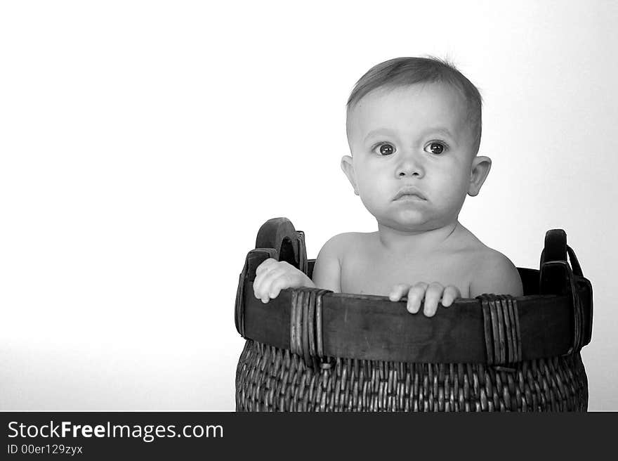 Black and white image of cute baby sitting in a woven basket. Black and white image of cute baby sitting in a woven basket