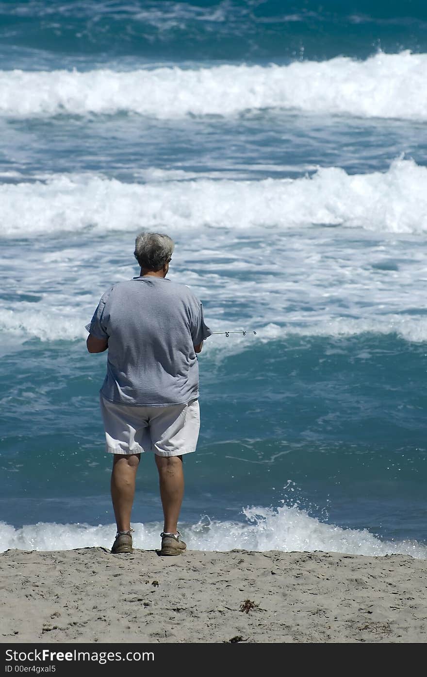 Man fishing in the surf with waves in background. Man fishing in the surf with waves in background