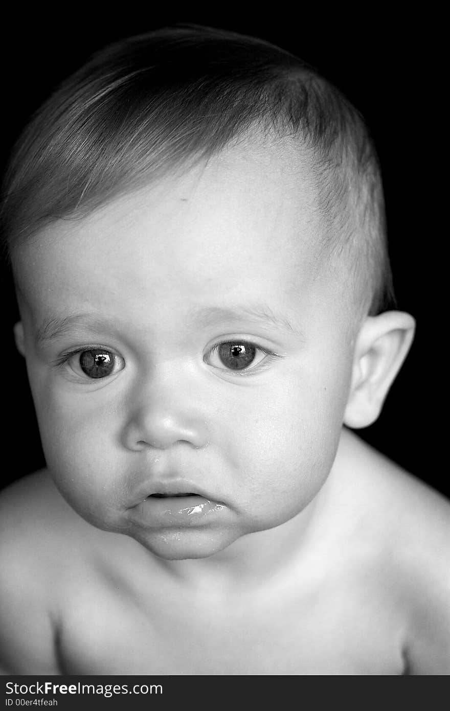 Black and white image of beautiful baby sitting in front of a black background