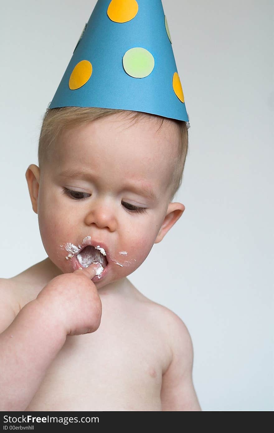 Image of an adorable 1 year old, wearing a paper hat, eating birthday cake. Image of an adorable 1 year old, wearing a paper hat, eating birthday cake