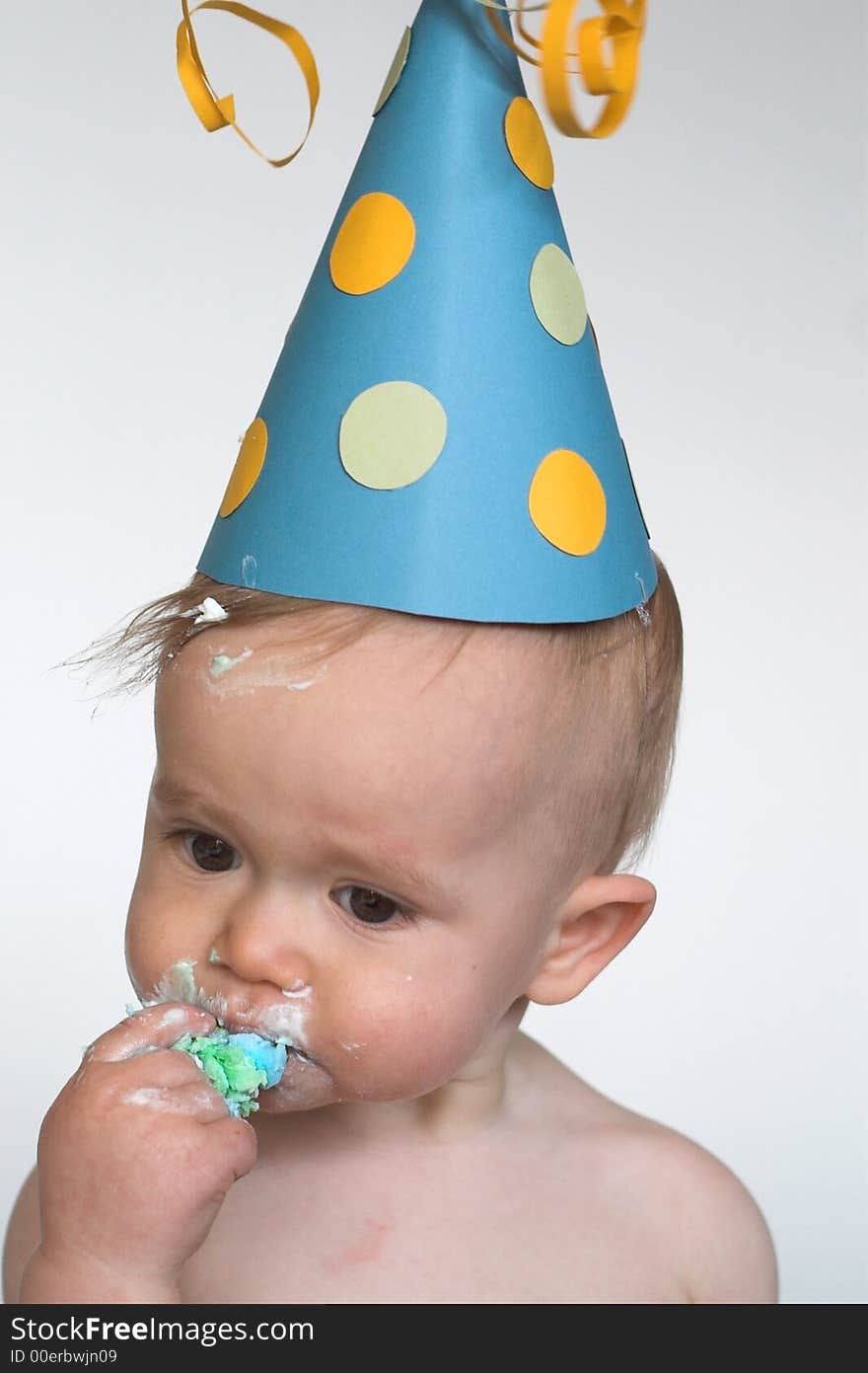 Image of an adorable 1 year old, wearing a paper hat, eating birthday cake. Image of an adorable 1 year old, wearing a paper hat, eating birthday cake