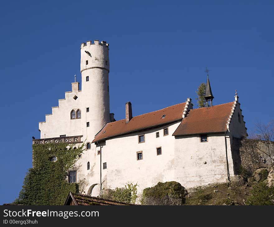 White castle with tower and main house in front of blue sky