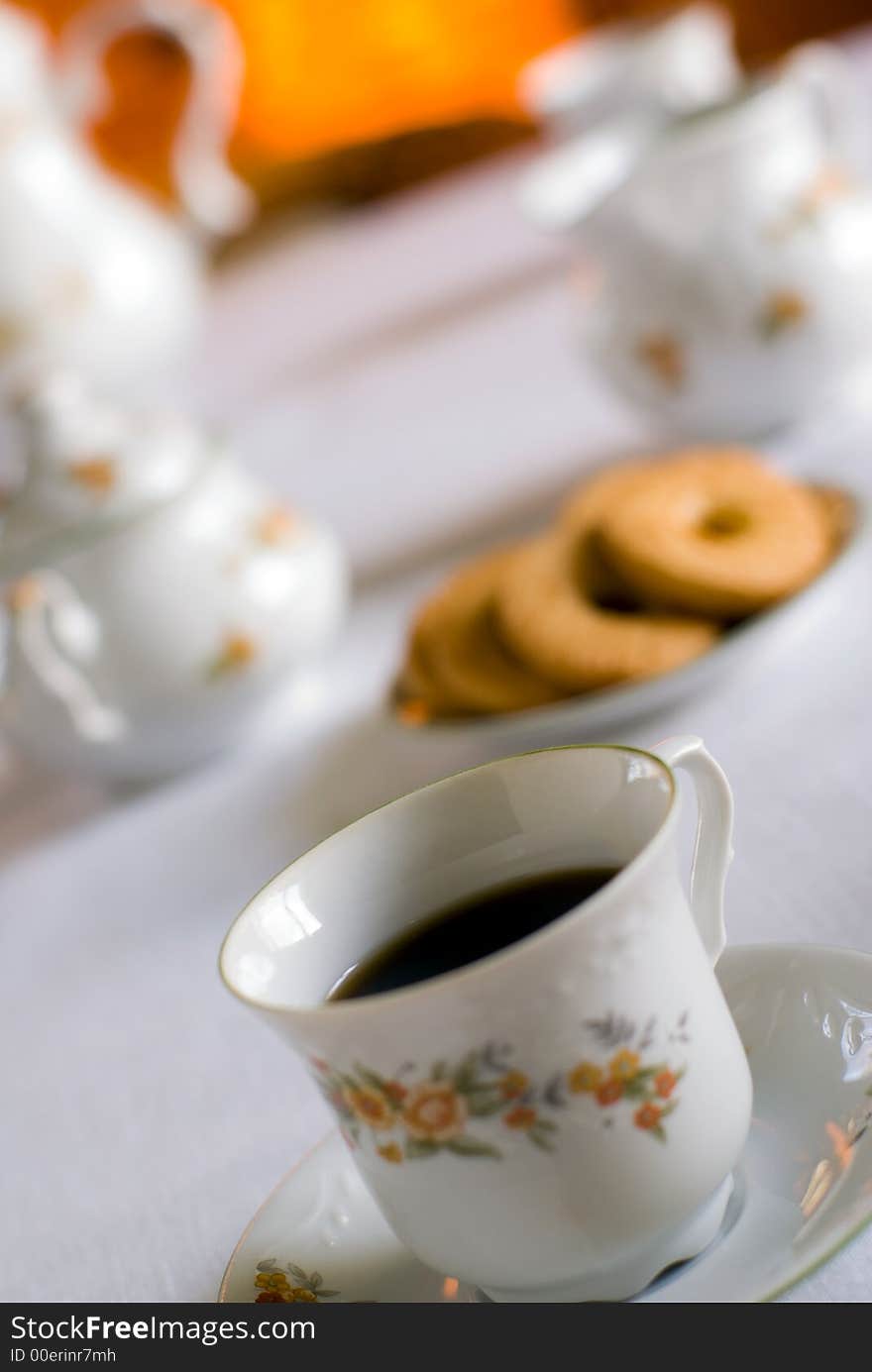 Coffee set on the table - cup of coffee on the front (shallow DOF focus on the liquid edge) cookies and milk jug, sugarl bowl behind.