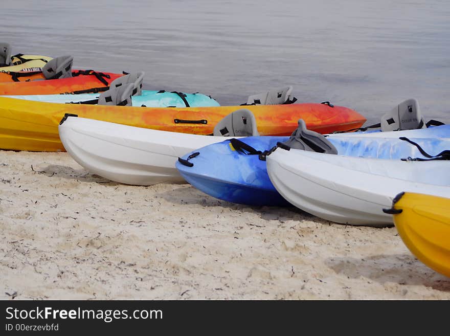 Colorful sea kayaks lined up on a sandy ocean shore.