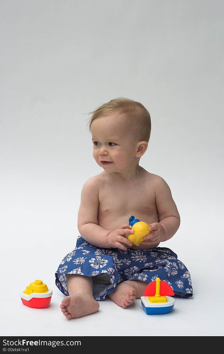 Image of an adorable baby wearing shorts, playing with toy boats. Image of an adorable baby wearing shorts, playing with toy boats