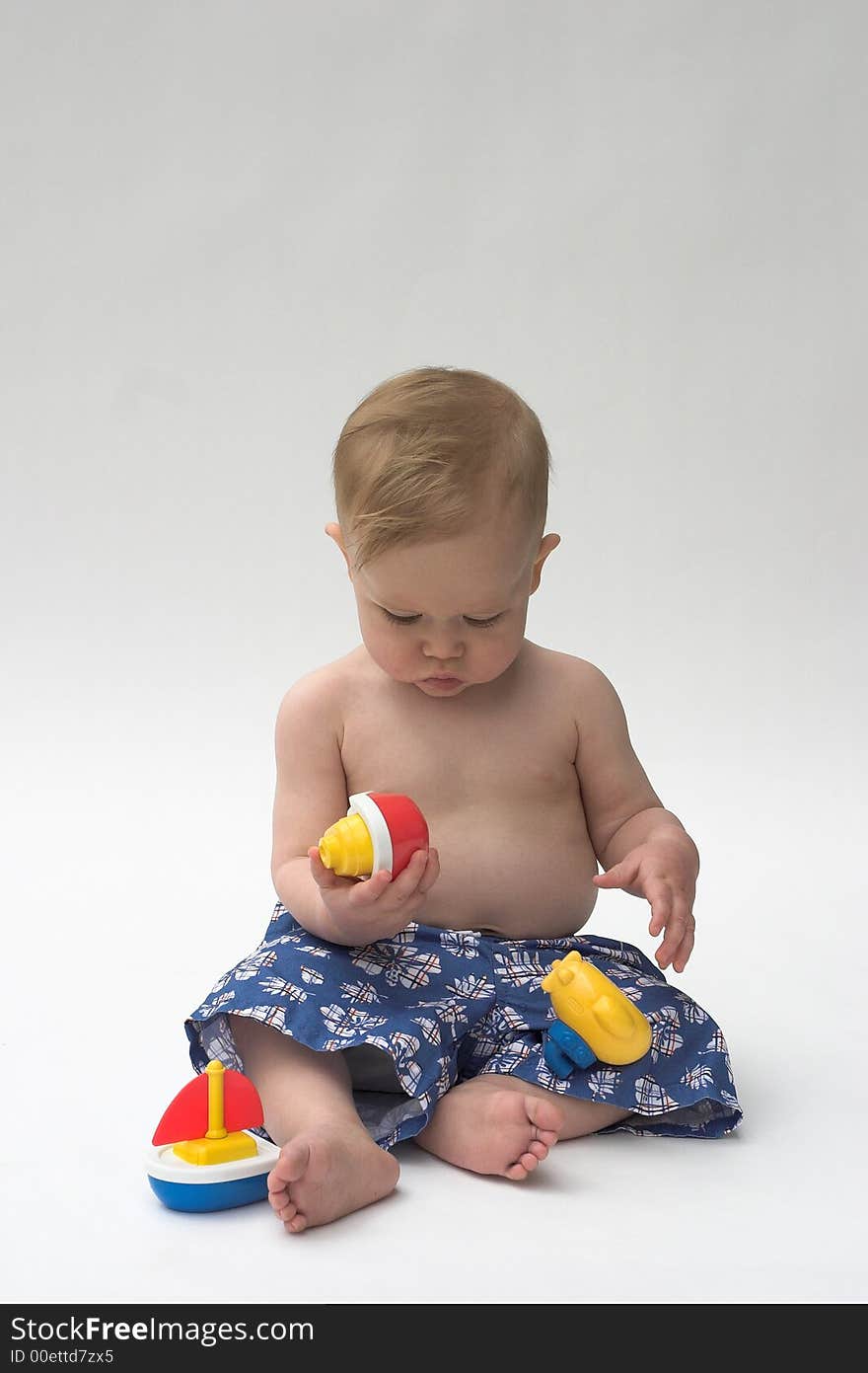 Image of an adorable baby wearing shorts, playing with toy boats. Image of an adorable baby wearing shorts, playing with toy boats