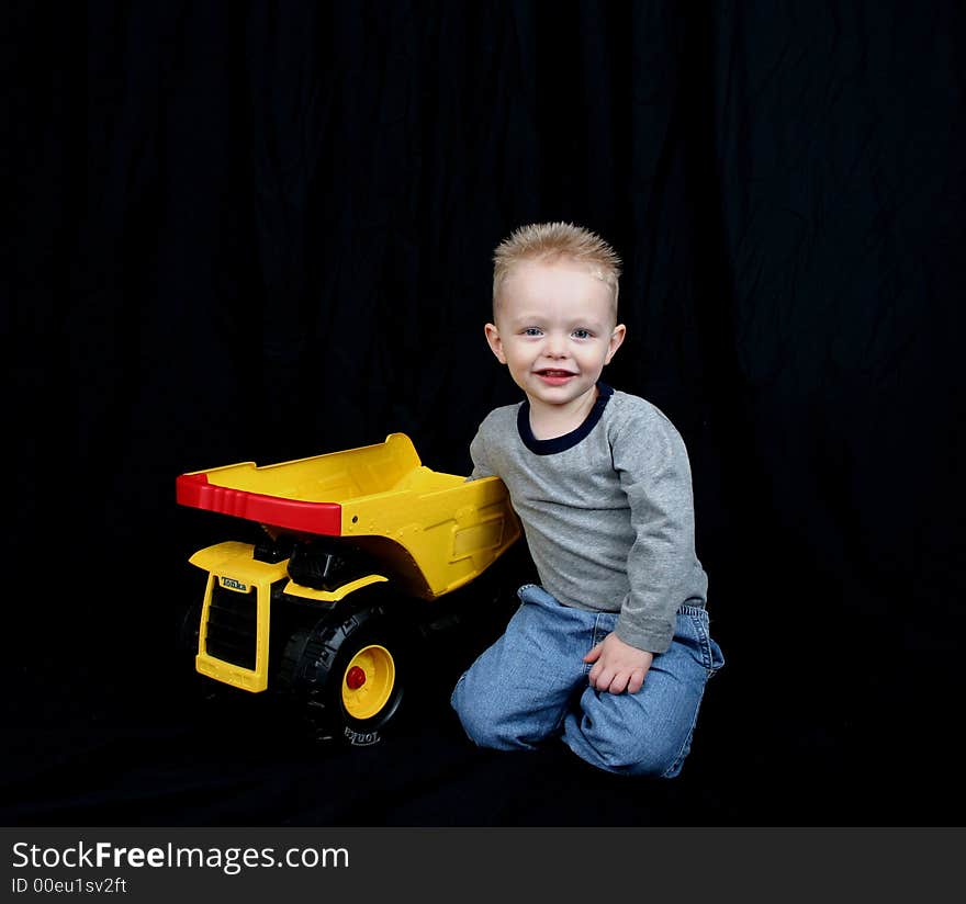 Cute little boy on black background with his truck