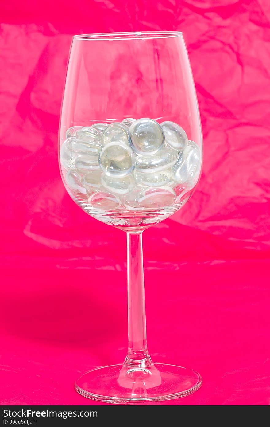 Sparkling stones in a wine glass on a red background. Sparkling stones in a wine glass on a red background