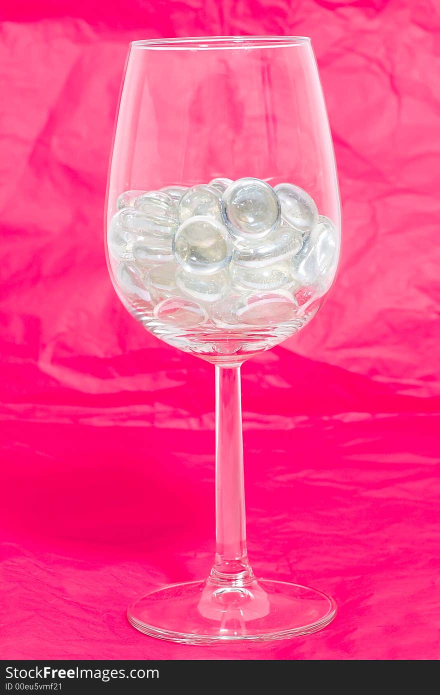 Sparkling stones in a wine glass on a red background. Sparkling stones in a wine glass on a red background