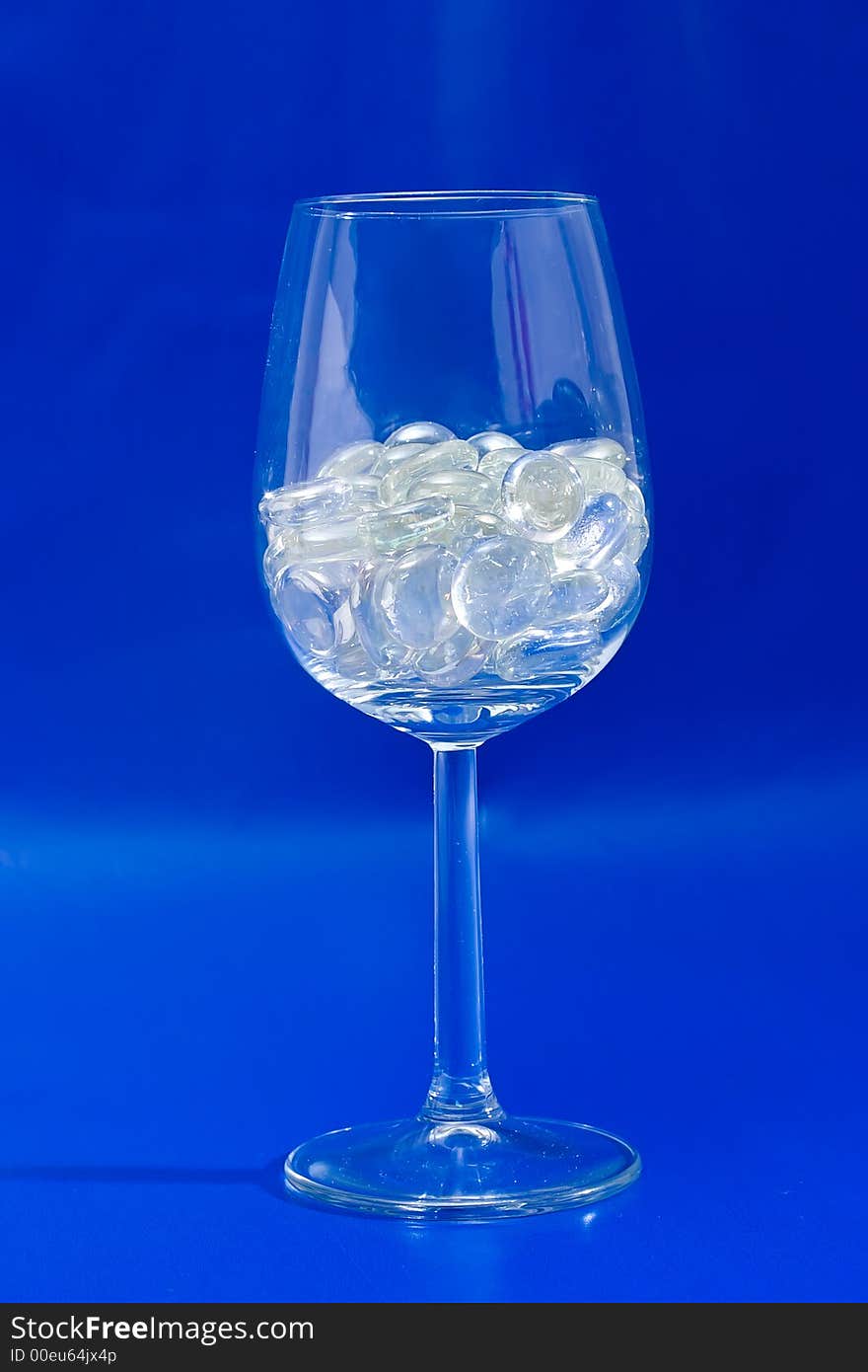 Wine glass with sparkling stones on a blue background. Wine glass with sparkling stones on a blue background