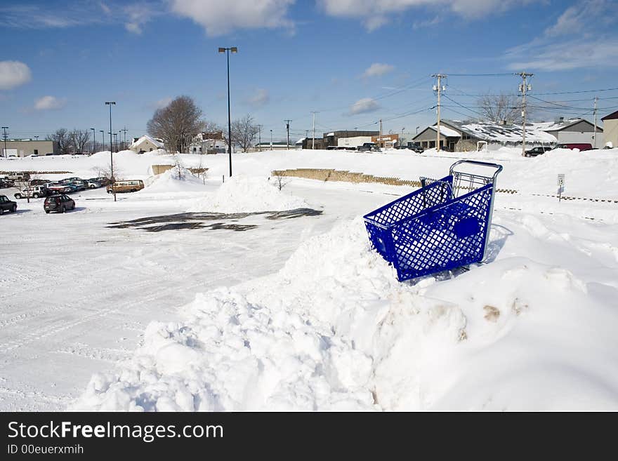 A shopping cart stuck at the top of a high snowbank by a retail parking lot. A shopping cart stuck at the top of a high snowbank by a retail parking lot.