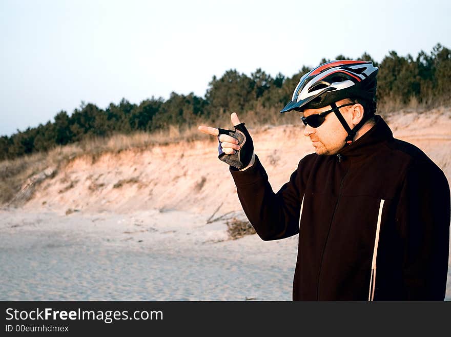 A man wearing a bike helmet, his hand in a pointing gesture. Sunglasses and gloves on. A man wearing a bike helmet, his hand in a pointing gesture. Sunglasses and gloves on.