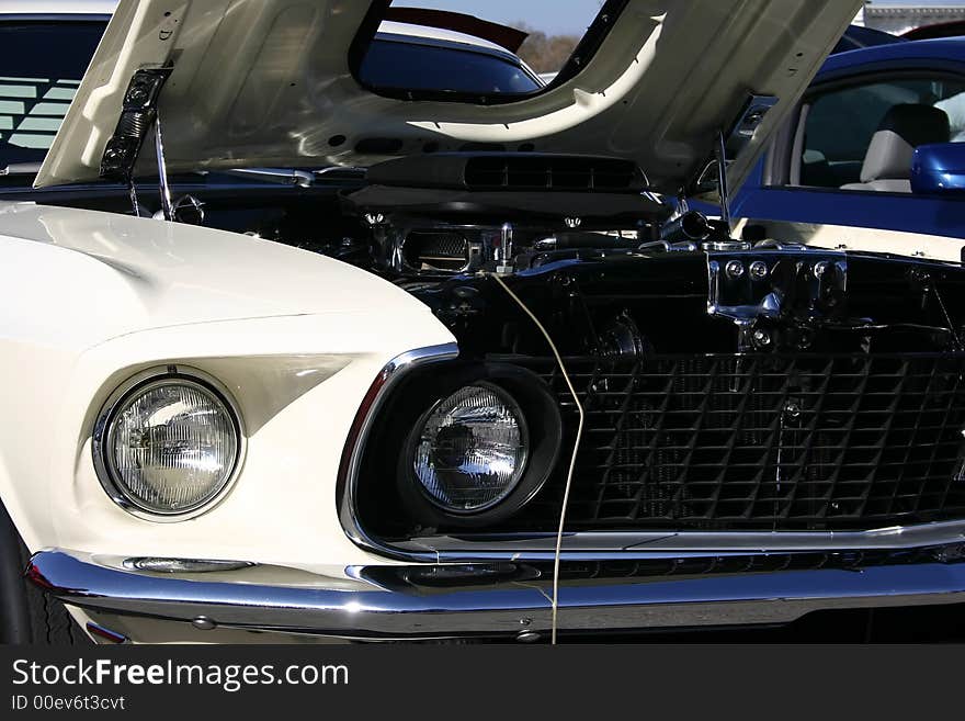 Closeup shot of a 1969 white Ford Mustang front end, shaker hood scoop, 428 Cobra Jet engine. Closeup shot of a 1969 white Ford Mustang front end, shaker hood scoop, 428 Cobra Jet engine.