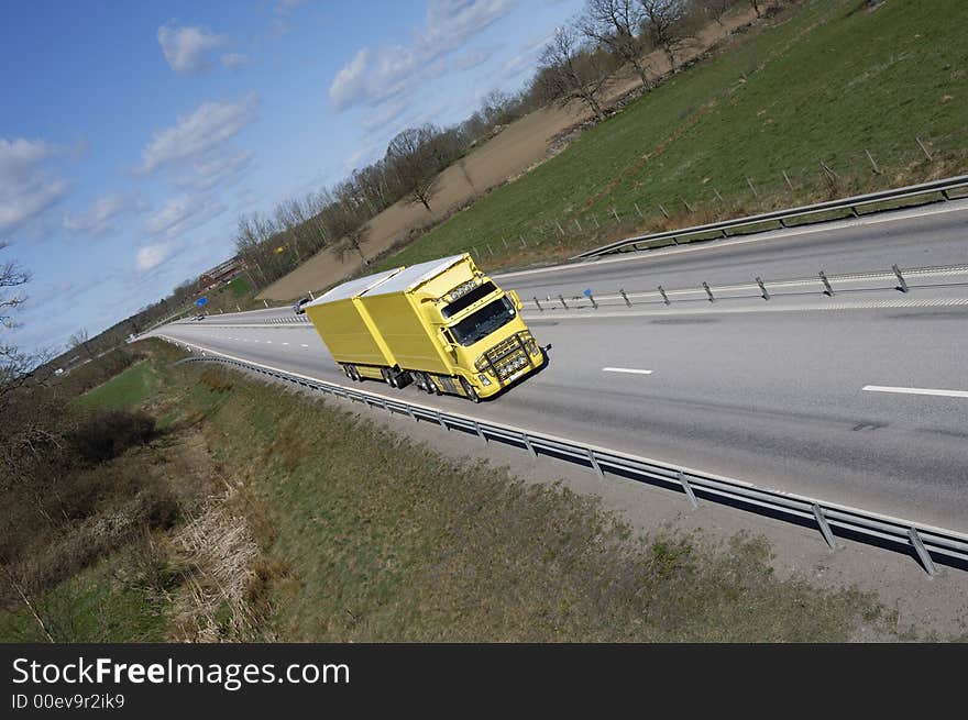 Large yellow truck speeding on long highway-straight. country-side in background. Large yellow truck speeding on long highway-straight. country-side in background