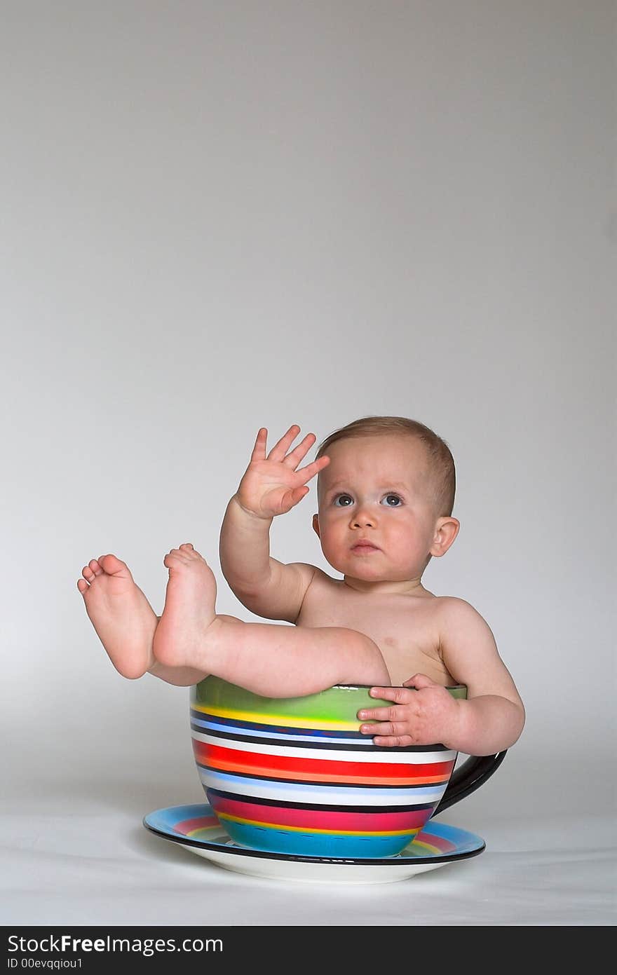 Image of an adorable baby sitting in a colorful, over-sized teacup. Image of an adorable baby sitting in a colorful, over-sized teacup