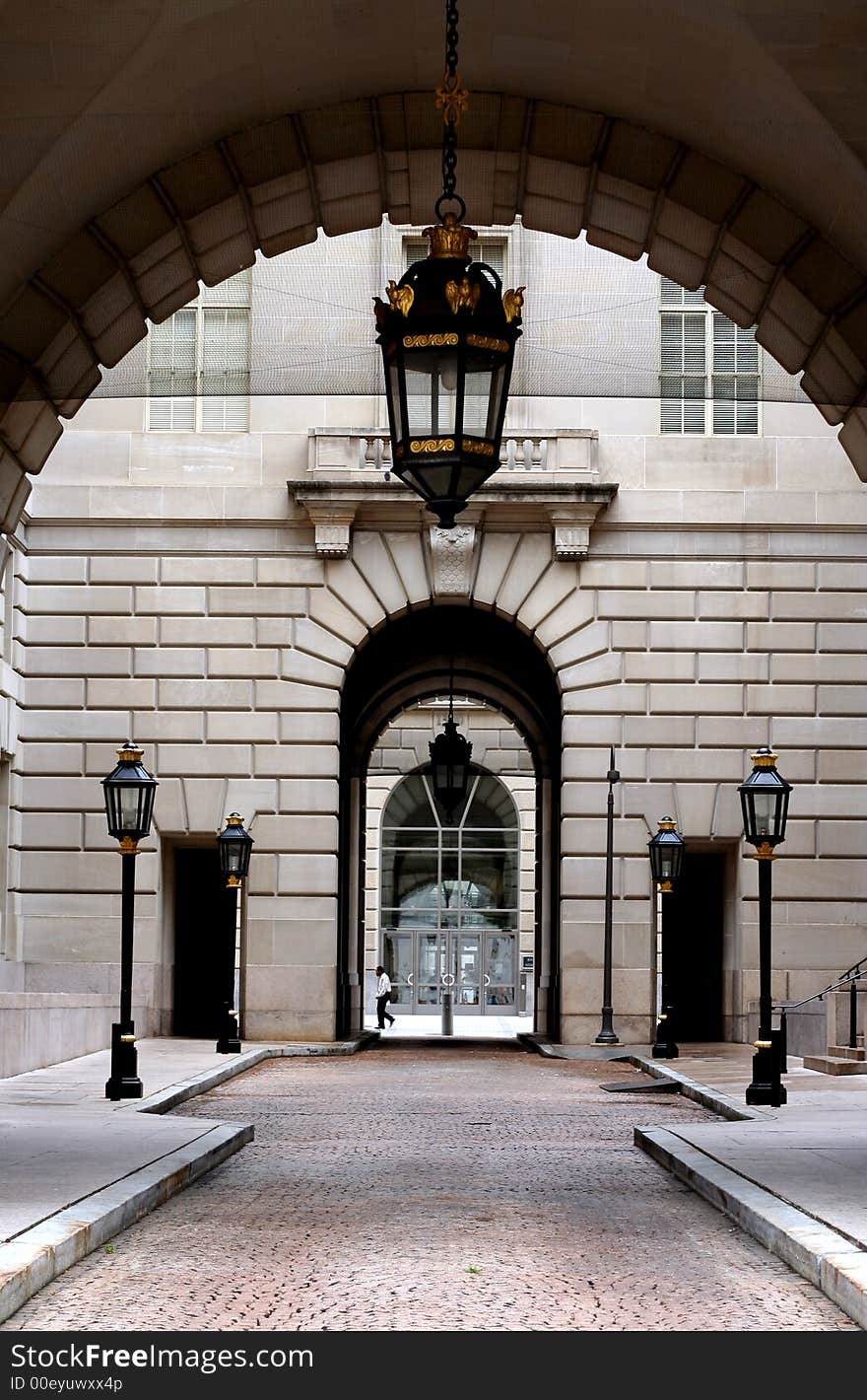 Arcs of a building with fancy streetlights in the inside court while a lone unidentifiable person in the background is walking.