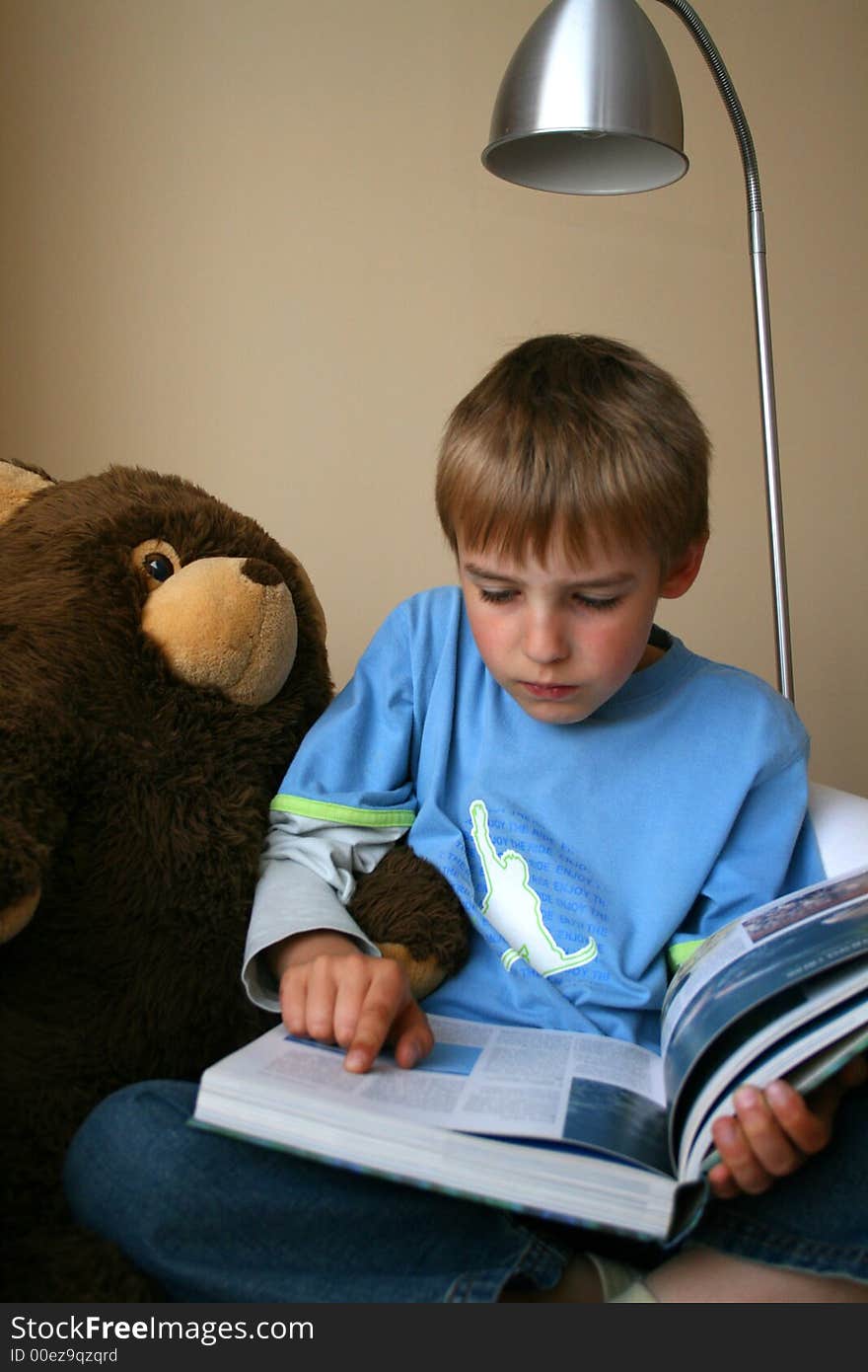 A small boy is reading interesting book with his teddy bear. A small boy is reading interesting book with his teddy bear