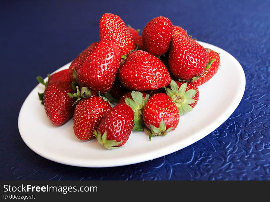 Hill of strawberries in white plate on a blue table-cloth