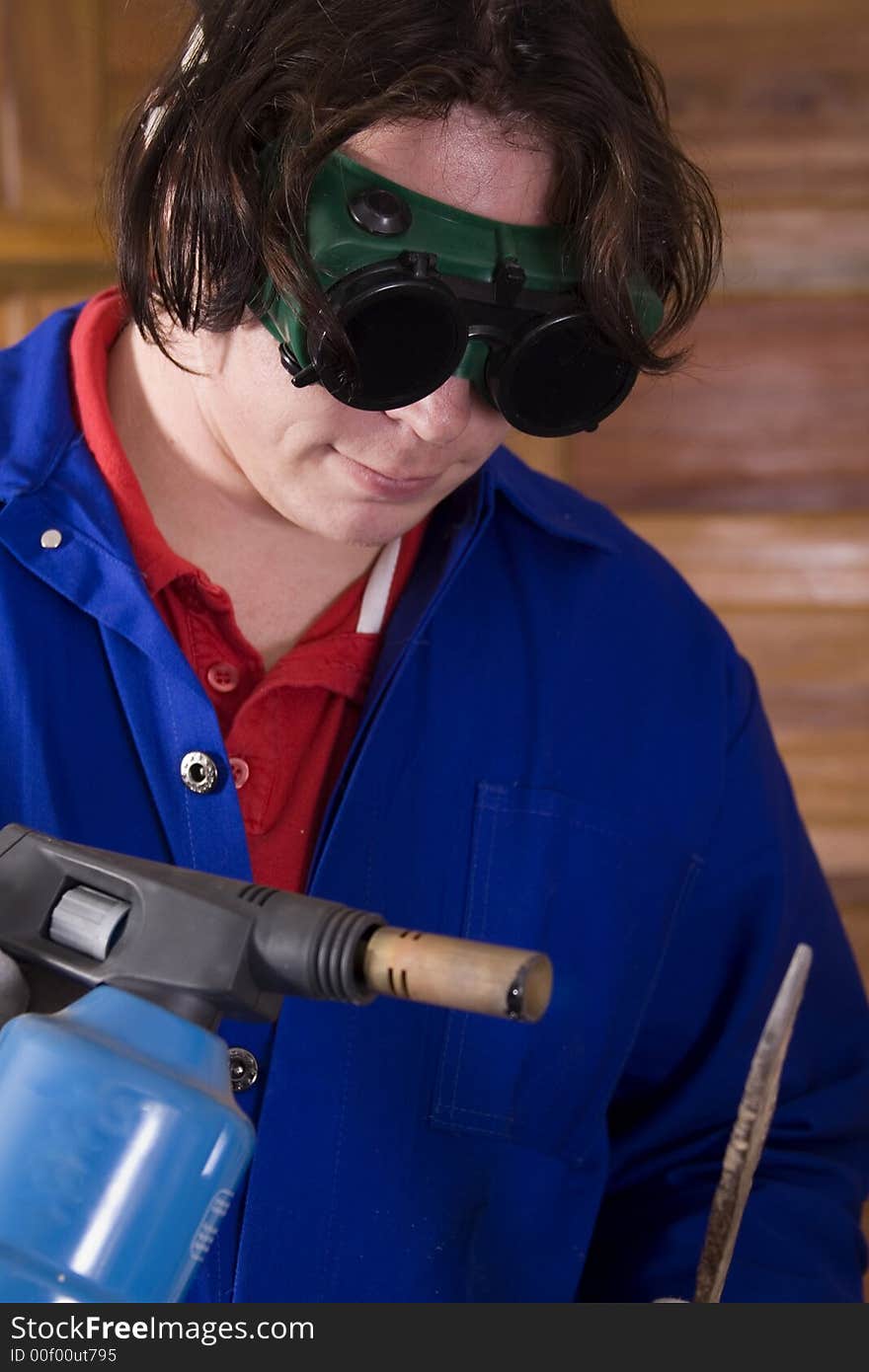 Dark haired man with blue overall holding blowtorch and metal. Dark haired man with blue overall holding blowtorch and metal