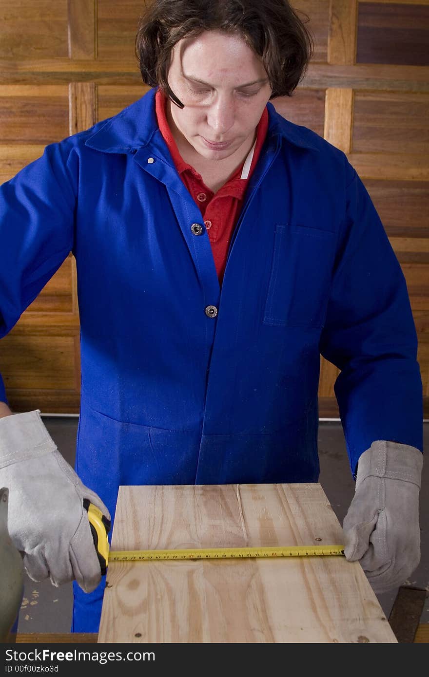 Dark haired man with blue overall measuring wood with gloves. Dark haired man with blue overall measuring wood with gloves