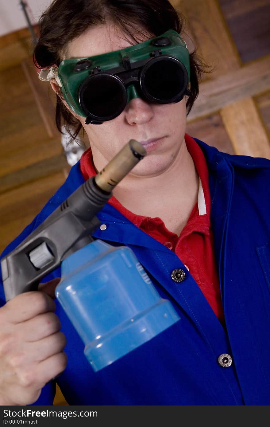 Dark haired man with blue overall holding blowtorch wearing welding goggles. Dark haired man with blue overall holding blowtorch wearing welding goggles