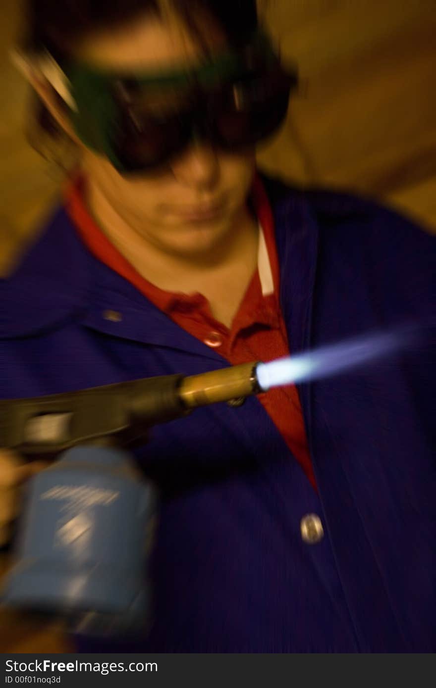 Dark haired man with blue overall holding blowtorch with radial blur. Dark haired man with blue overall holding blowtorch with radial blur