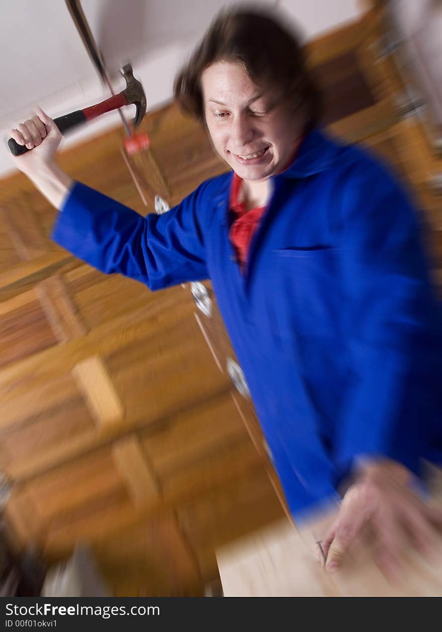 Dark haired man with blue overall holding hammer about to hit nail. Dark haired man with blue overall holding hammer about to hit nail