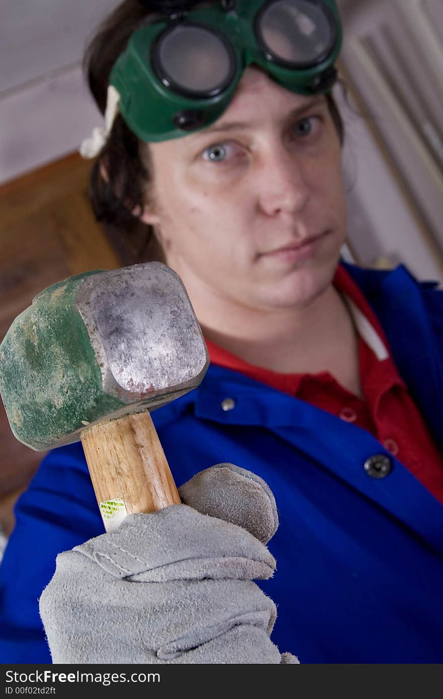 Dark haired man with blue overall holding hammer (focus on the hammer). Dark haired man with blue overall holding hammer (focus on the hammer)