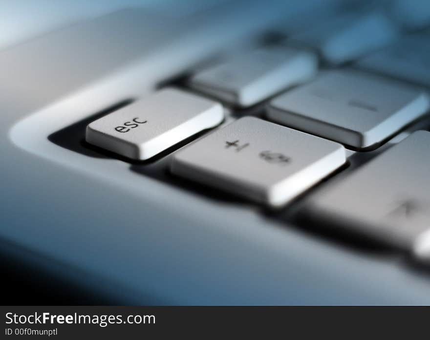 Close-up of laptop keyboard with focus on escape key. Blue lighting effect added with clear patch on escape key. Close-up of laptop keyboard with focus on escape key. Blue lighting effect added with clear patch on escape key.