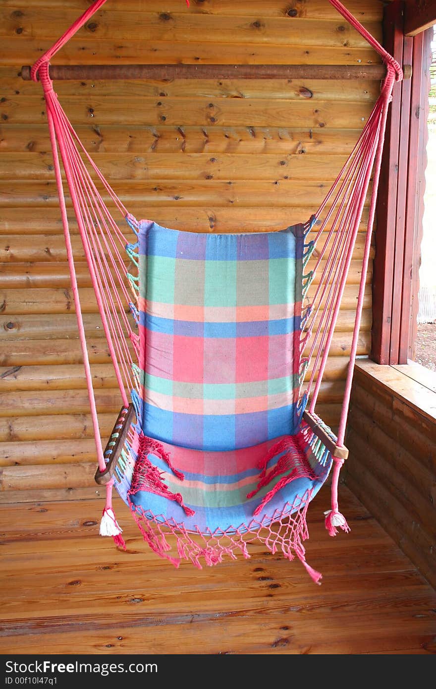 A colorful swing hanging on the porch of a wood cabin. A colorful swing hanging on the porch of a wood cabin