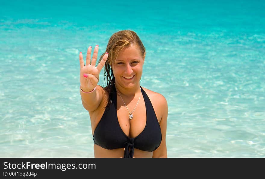 Young woman in black bikini showing the number four with the fingers of her right hand. Background is of clear blue water. Young woman in black bikini showing the number four with the fingers of her right hand. Background is of clear blue water.