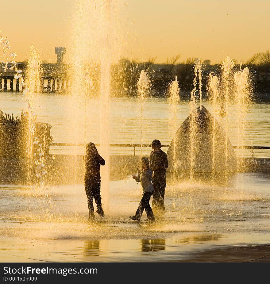 Three kids cool of in water fountain at sunset, no faces visable. Three kids cool of in water fountain at sunset, no faces visable