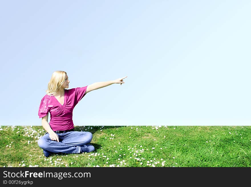 A young woman is sitting on a green meadow and show something. A young woman is sitting on a green meadow and show something