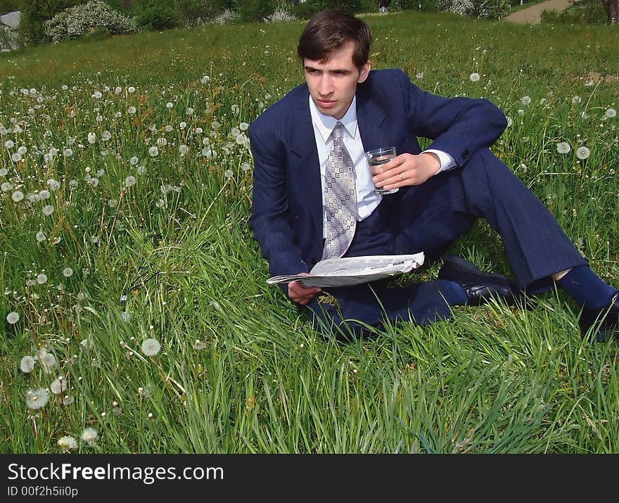 Young businessman sits on a lawn and holds newspaper. Young businessman sits on a lawn and holds newspaper