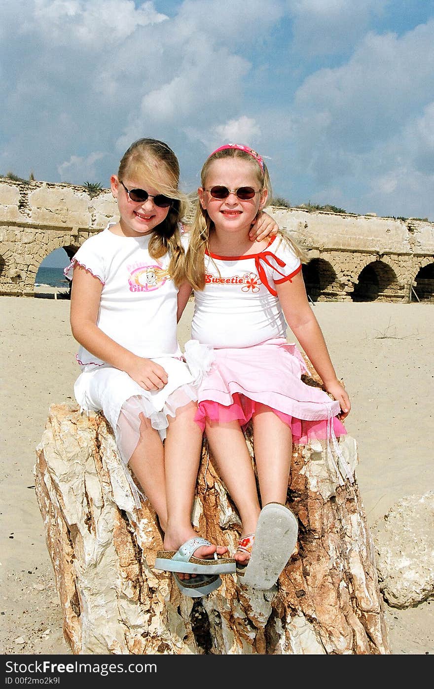 Girls twins sit on a stone in dark glasses. Girls twins sit on a stone in dark glasses