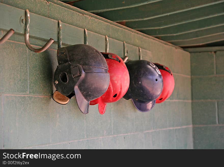 Old blue and red batting helmets hanging in a dugout