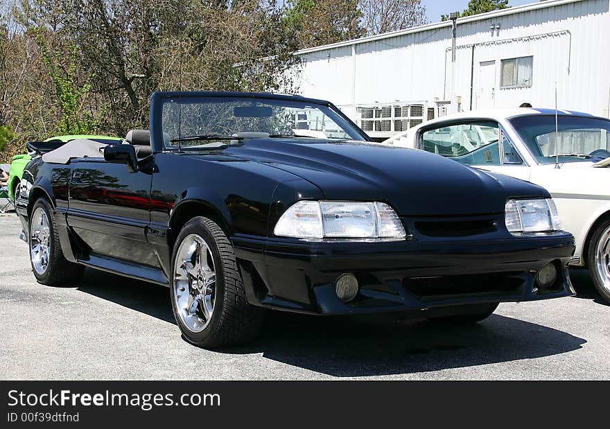 1993 Ford Mustang convertible. Black car with clear headlamps, cowl hood and chrome wheels.