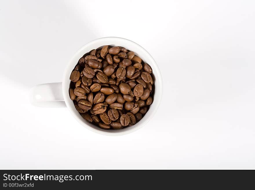 White mug, filled with good smelling coffeebeans on white background. View from above. White mug, filled with good smelling coffeebeans on white background. View from above.