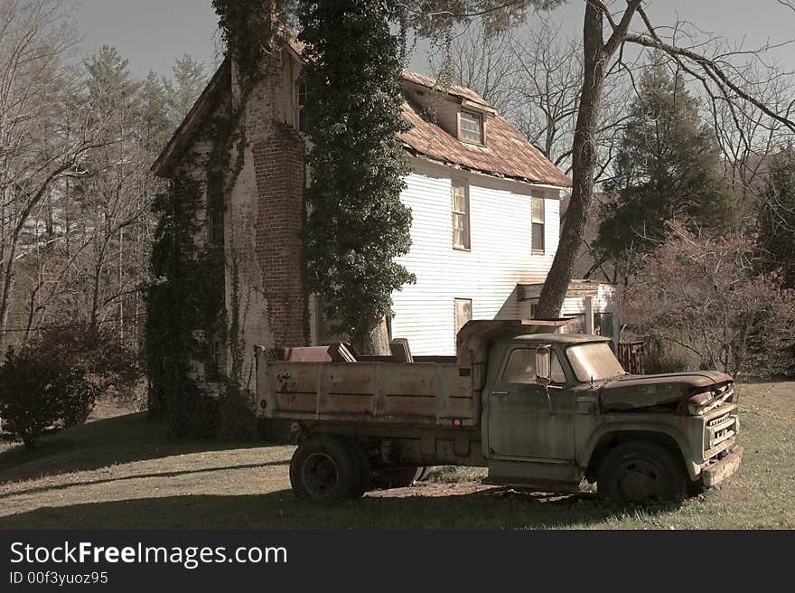 Antique dump truck in front of abandoned house, sepia tone