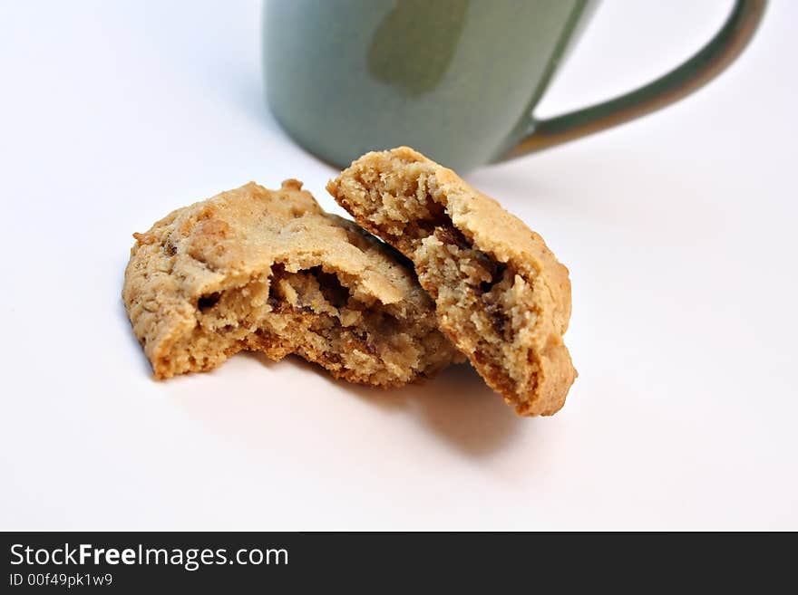 A cookie broken in half with a green coffee cup in the background isolated on white. A cookie broken in half with a green coffee cup in the background isolated on white